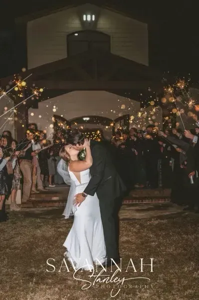 Newlyweds kissing at a candlelit church entrance surrounded by sparklers and guests