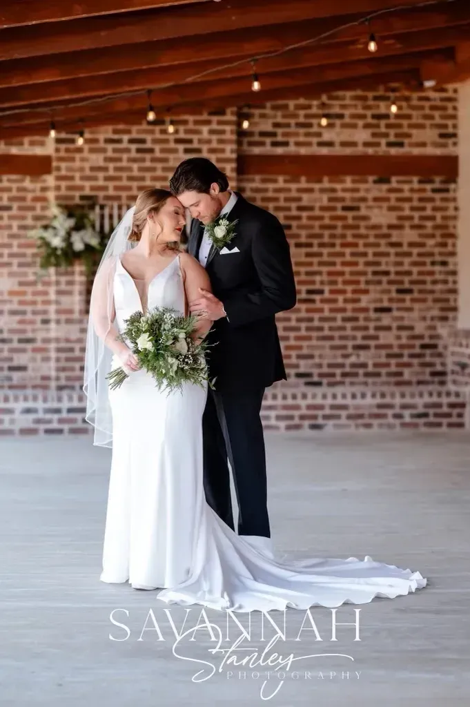 Bride and groom kissing in a brick-walled indoor venue, bride in white gown holding bouquet
