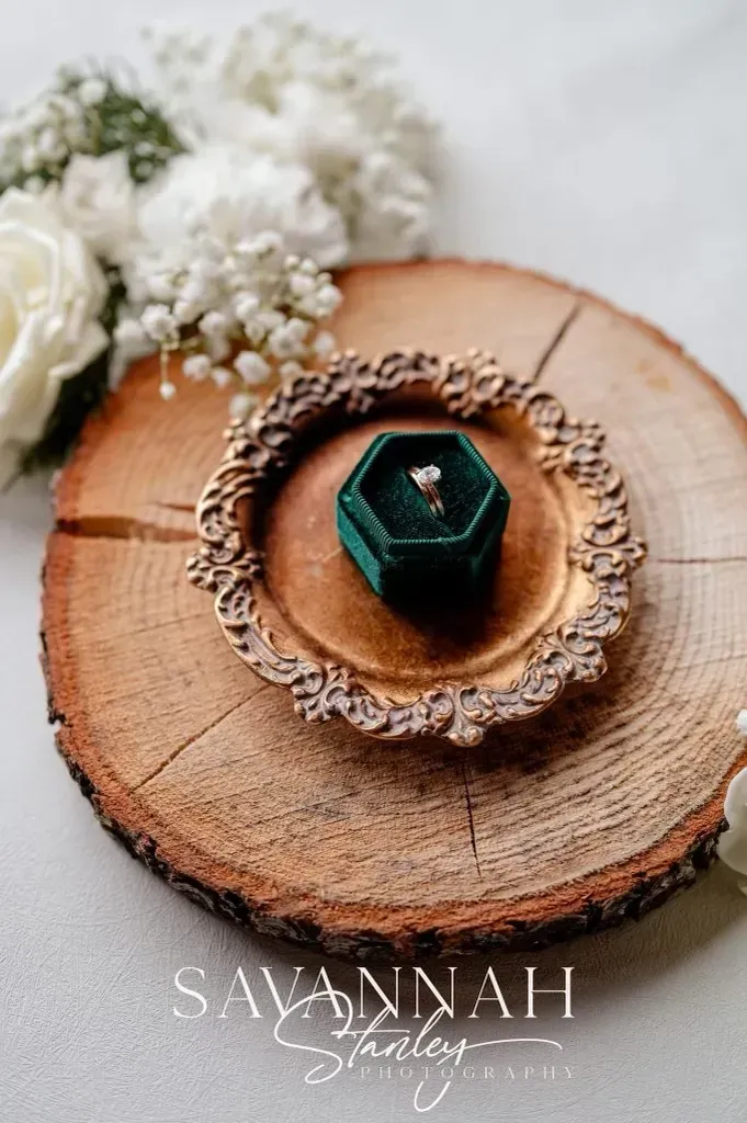 Teal gemstone ring on a rustic wooden slice with white flowers and decorative lace trim