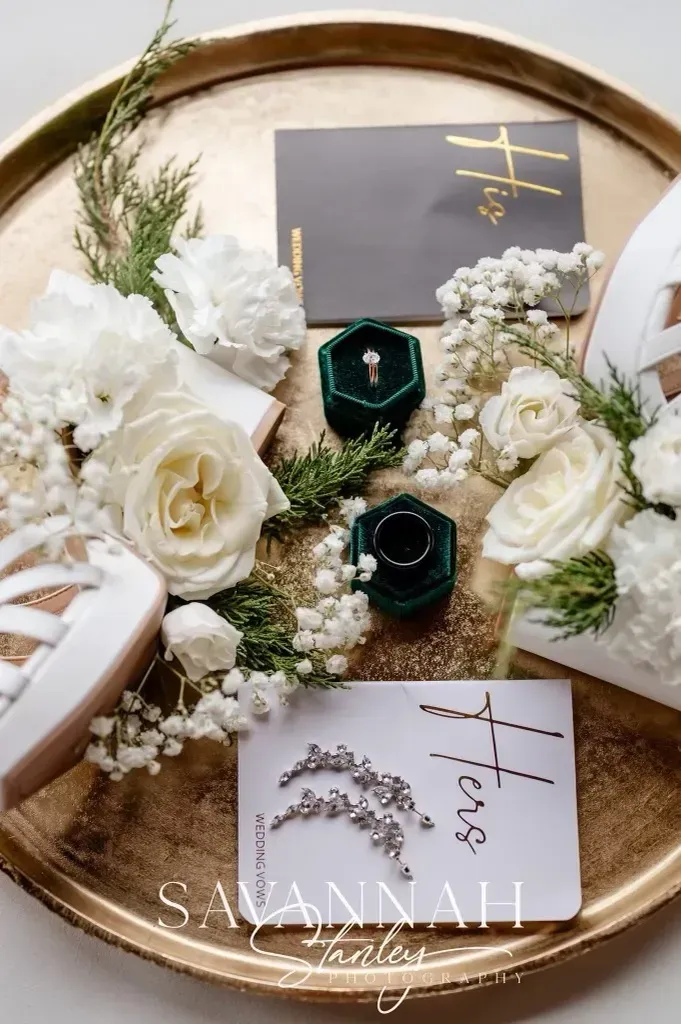 Elegant floral gift tray with white roses, greenery, and two green rings on a gold-rimmed platter.