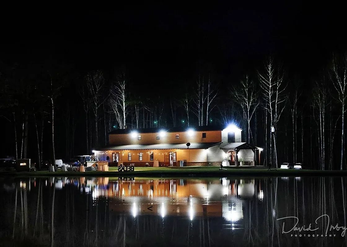 Lit cabin by a dark lake at night, with trees and bright reflections on the water.