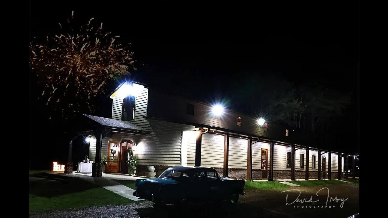 Nighttime view of a lit restaurant with fireworks bursting above and cars parked outside.