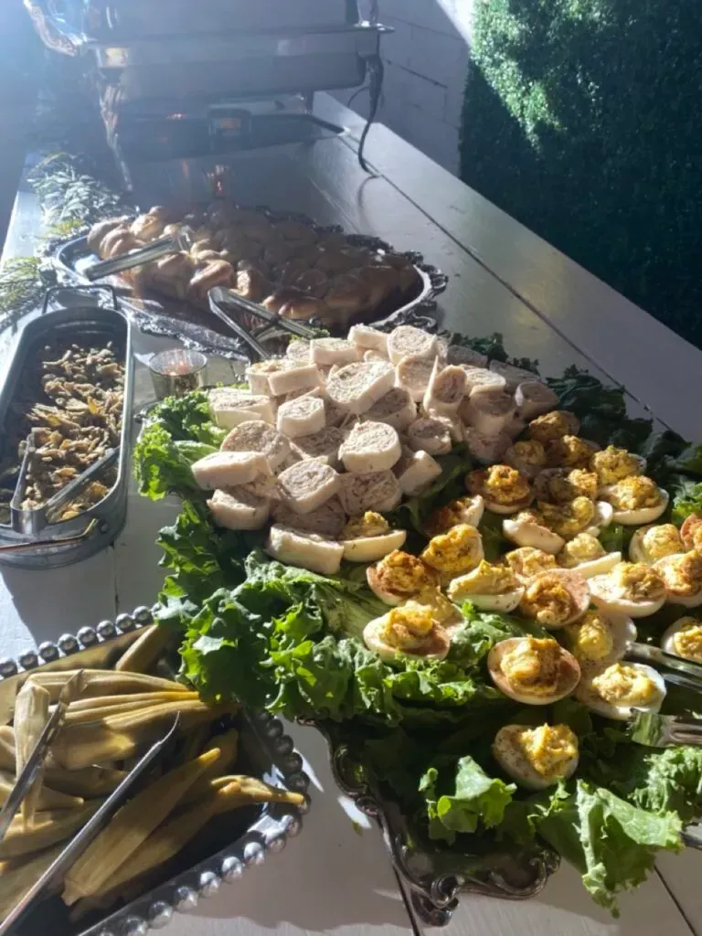 Buffet table with assorted appetizers, sliced bread, and leafy garnishes under dim lighting