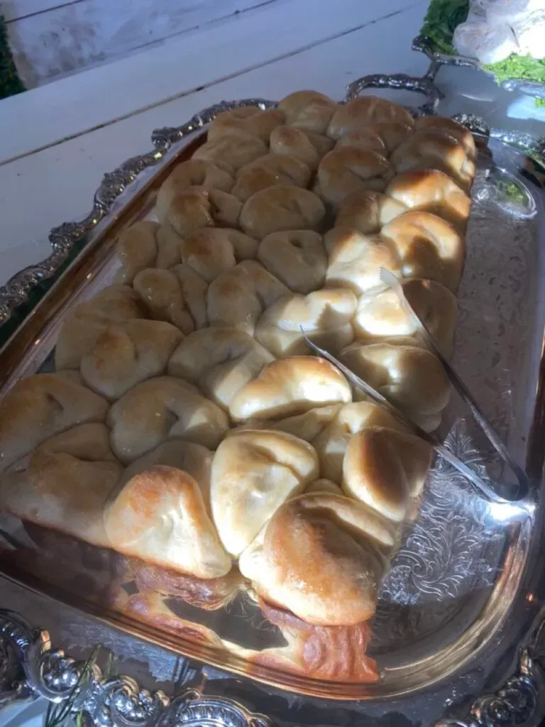 Tray of golden-brown bread rolls on a foil-lined serving platter in sunlight