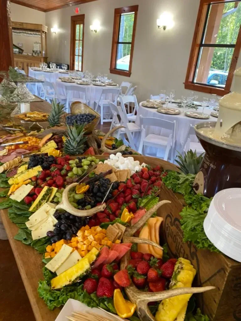 Large fruit and cheese platter on a table in a bright dining room with white chairs and set tables