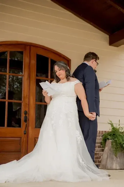 Bride and groom stand back-to-back on a porch, reading letters in formal wedding attire.
