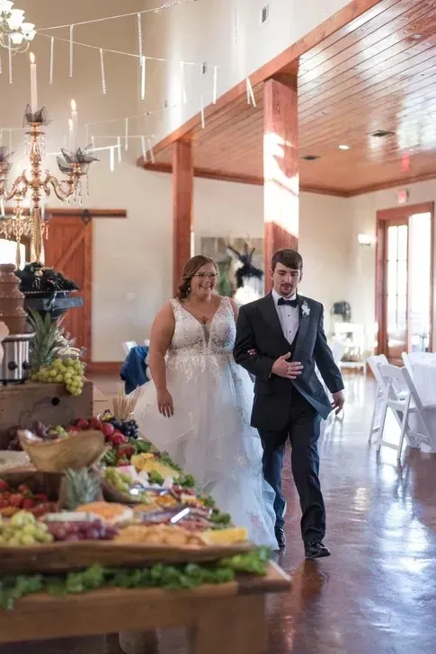 Bride and groom walking through a bright reception hall beside a buffet table