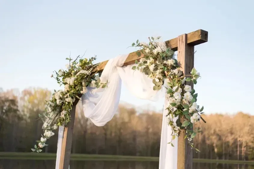 White draped wedding arch with greenery outdoors at sunset