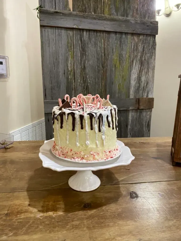 Chocolate-drip cake with pink frosting on a white pedestal stand on a wooden table