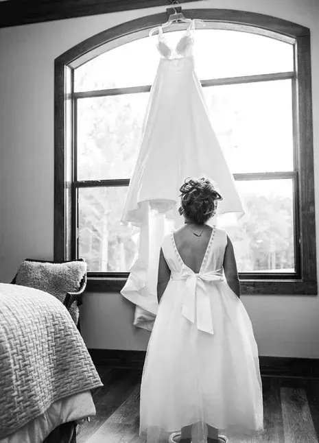 White dress hanging by a window above a young girl in a bright room