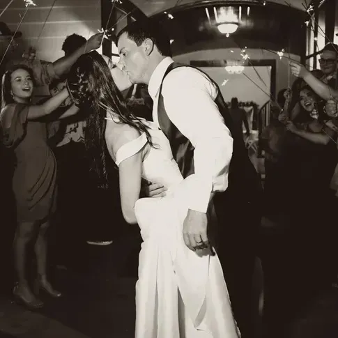 Couple dancing closely at a lively indoor party, surrounded by cheering guests.