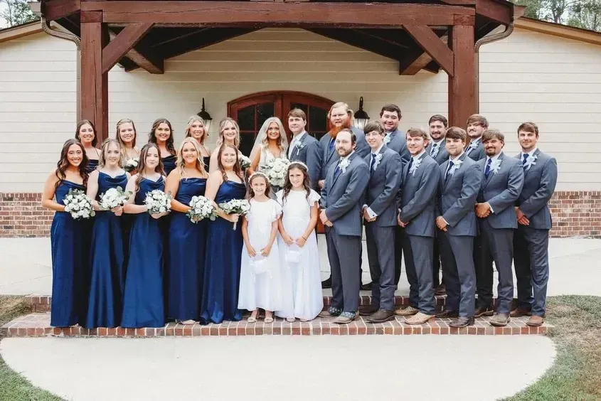 Wedding party posing on steps outside a venue, bridesmaids in navy, groomsmen in gray, and bride in white.