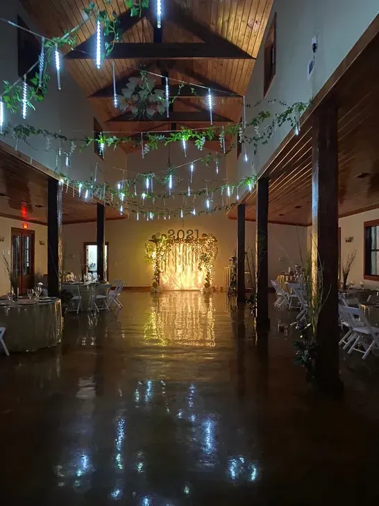 Decorated indoor event hall with string lights, reflective floor, and glowing backdrop at the far end