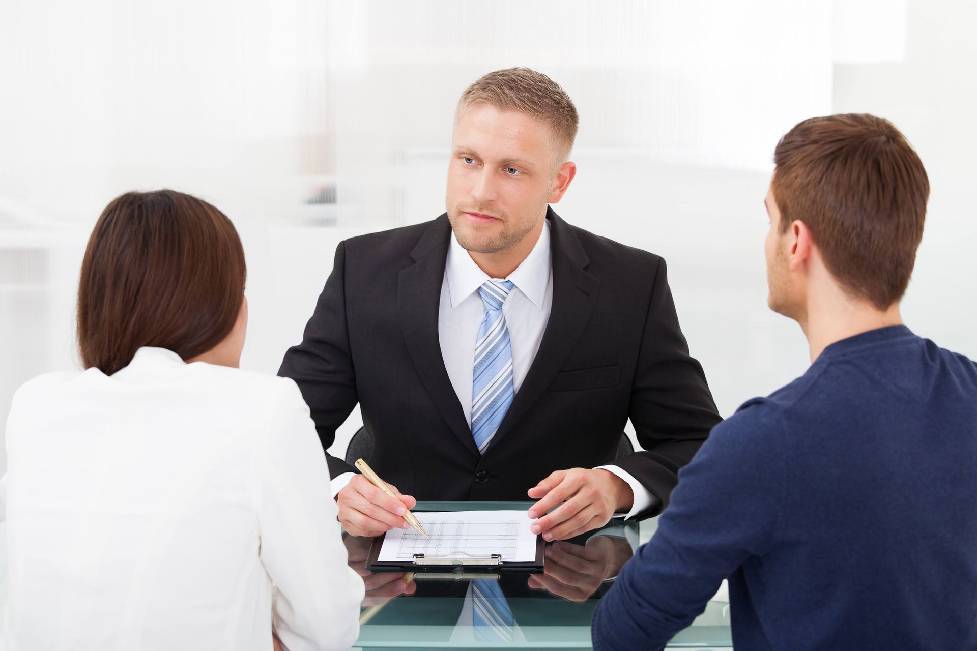 A man in a suit advises a couple at a desk, reviewing documents.