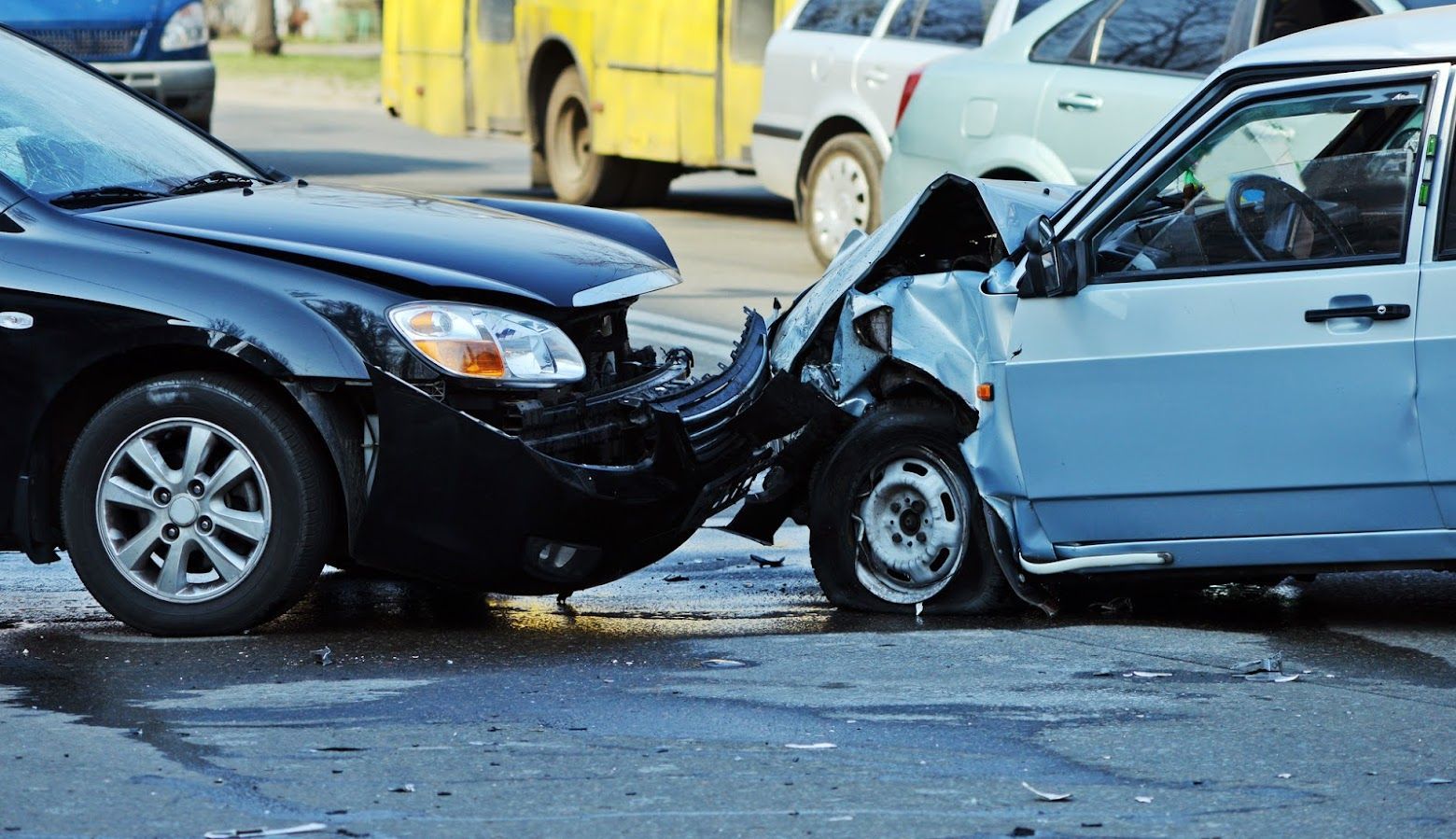 Two cars damaged in a head-on collision on a street. Black car and blue car with heavy front-end damage.