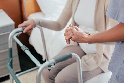 Person using a walker with assistance from a caregiver, indoors.