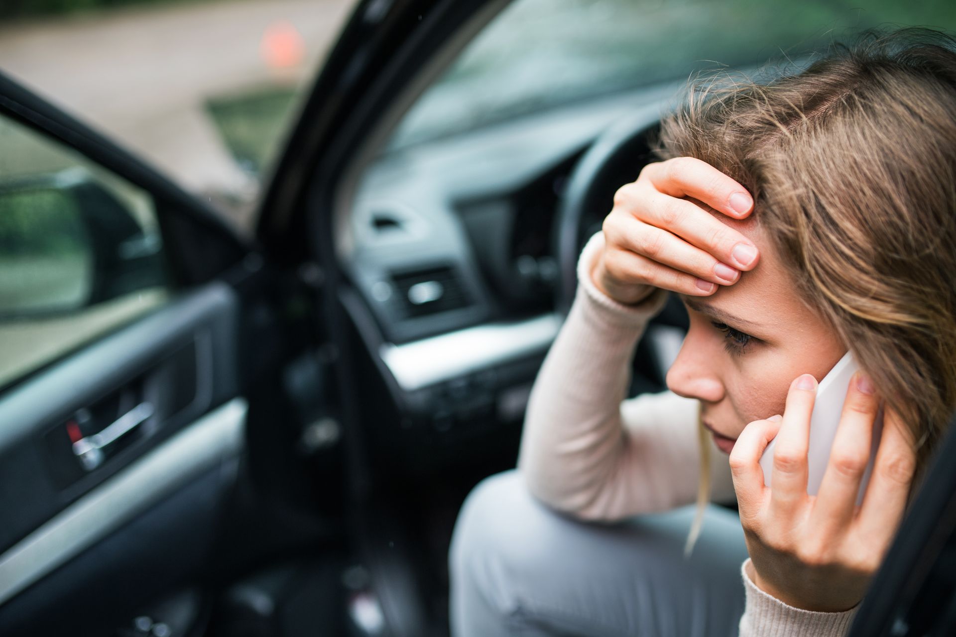 Woman sitting in a car, looking distressed while talking on a cellphone