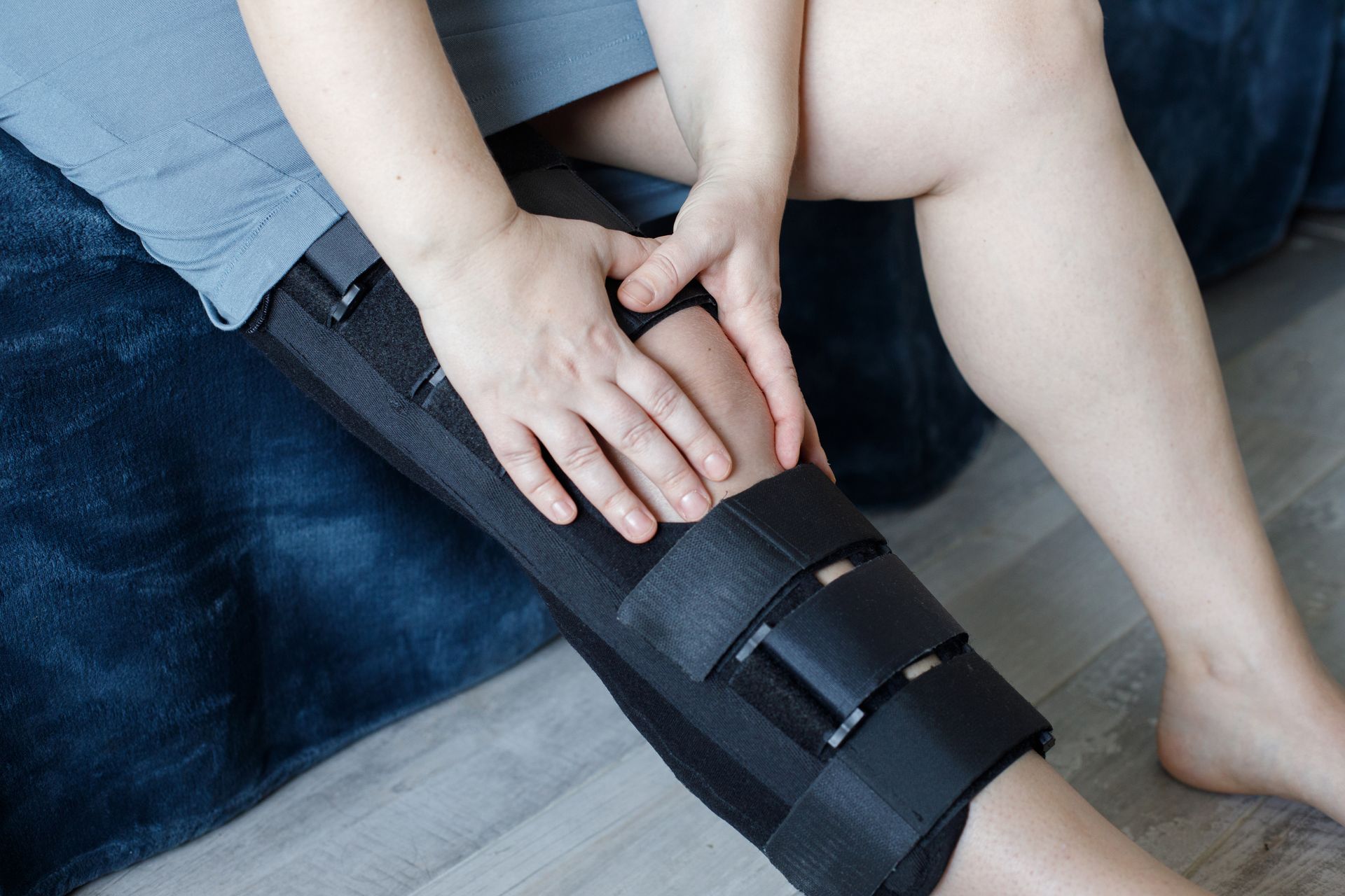Person wearing a knee brace while holding an injured knee during recovery