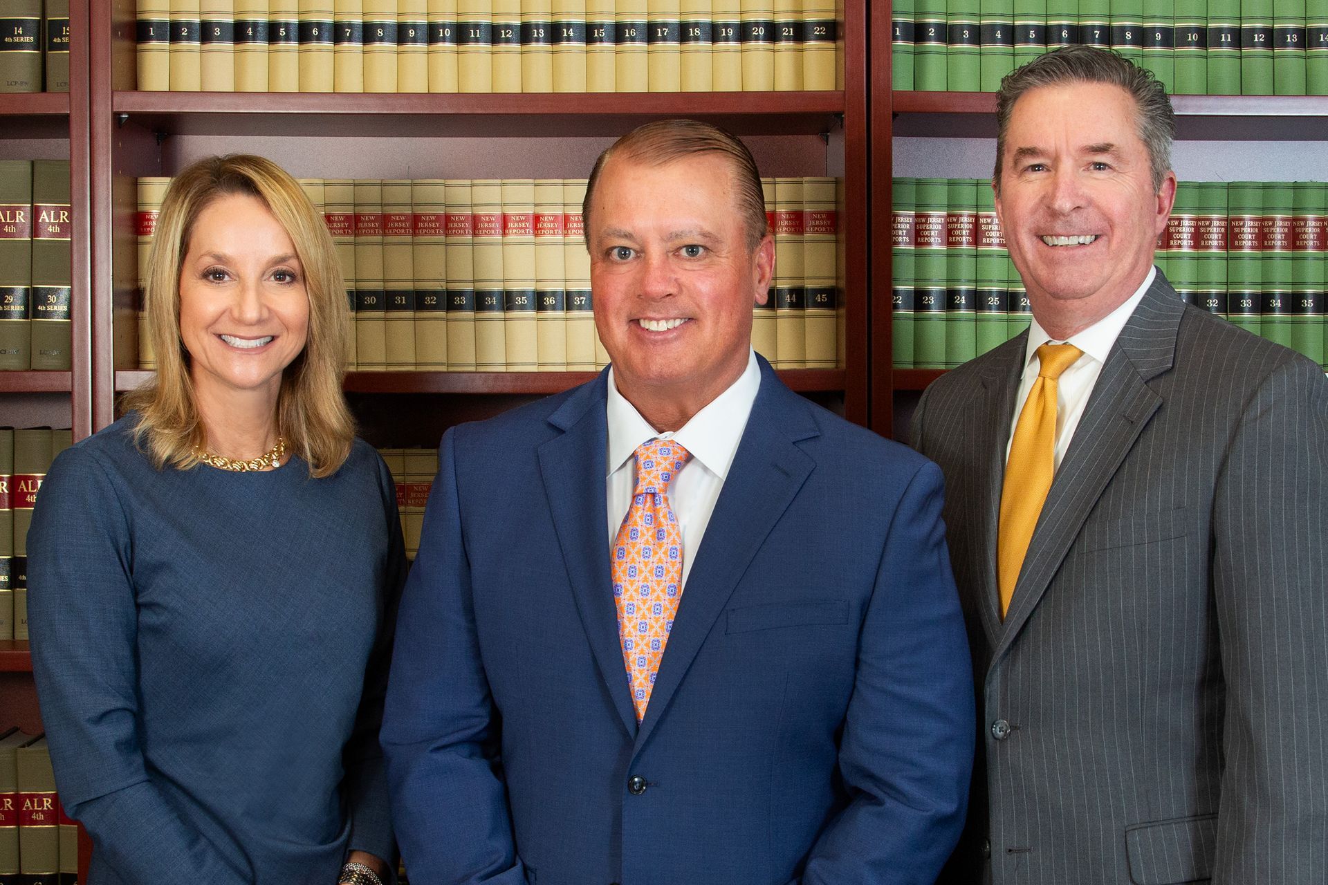 Three people in business attire in front of a bookshelf. Two men and one woman smiling.
