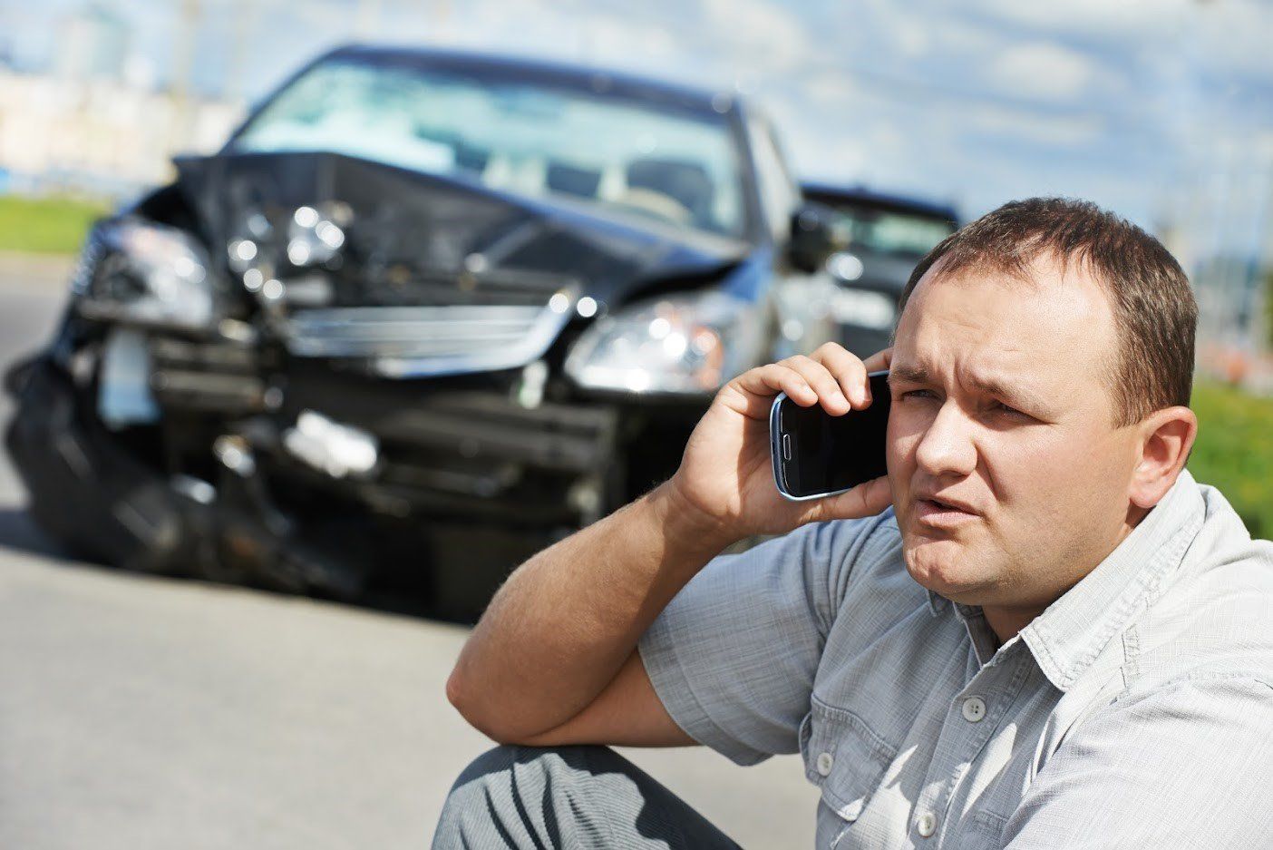 Man on phone beside a damaged black car after an accident on the road.