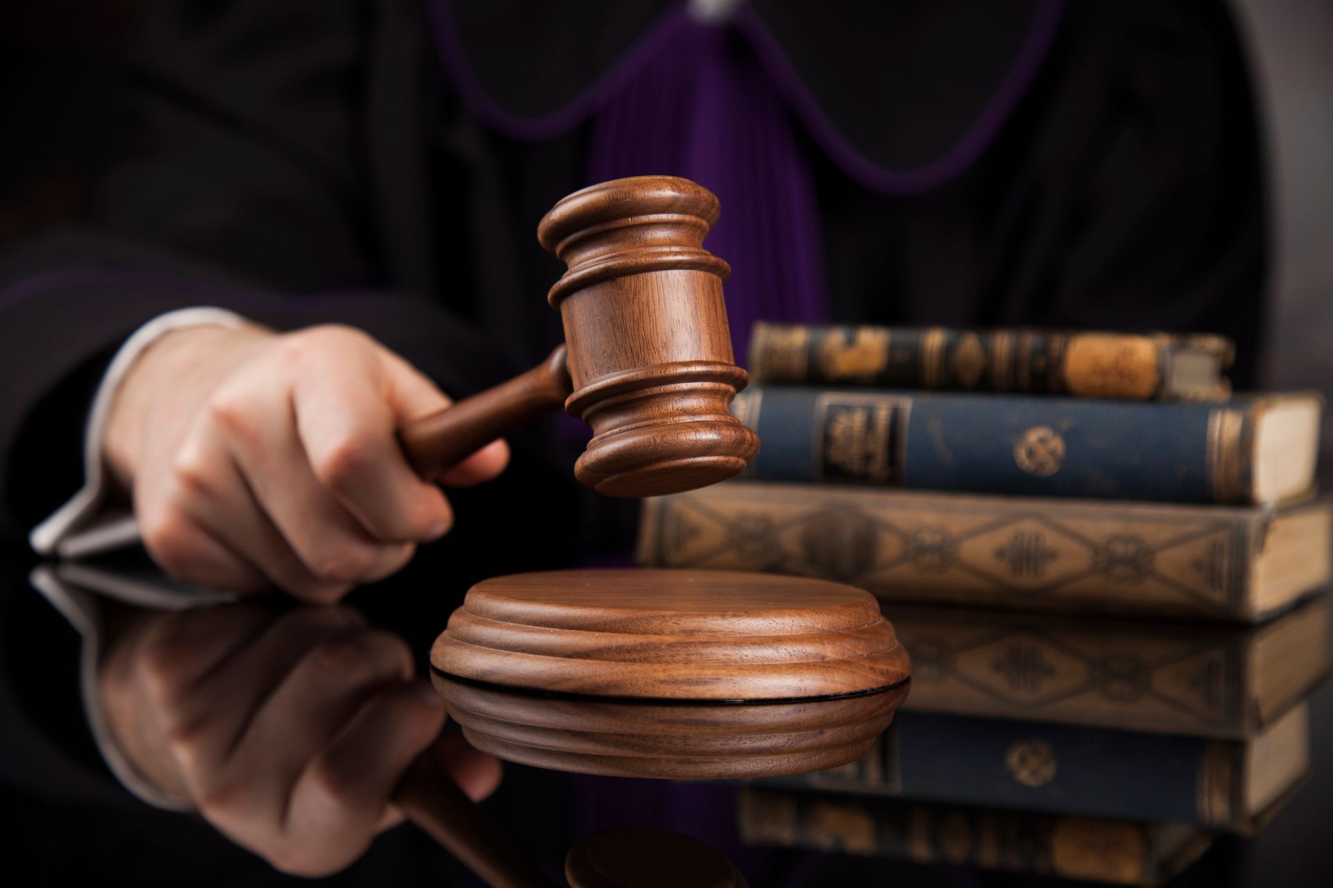 Judge holding gavel over a wooden block, with law books in the background.
