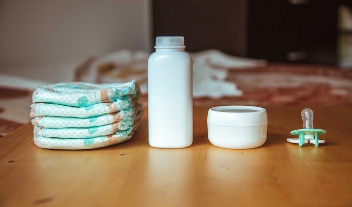 Pile of diapers, bottle, jar, and pacifier on a wooden surface.