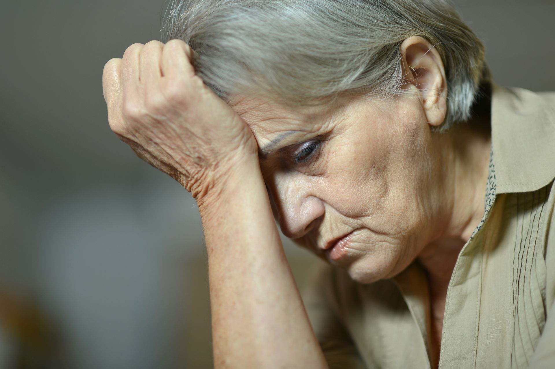 Woman with gray hair, hand on forehead, looking down, showing sadness.