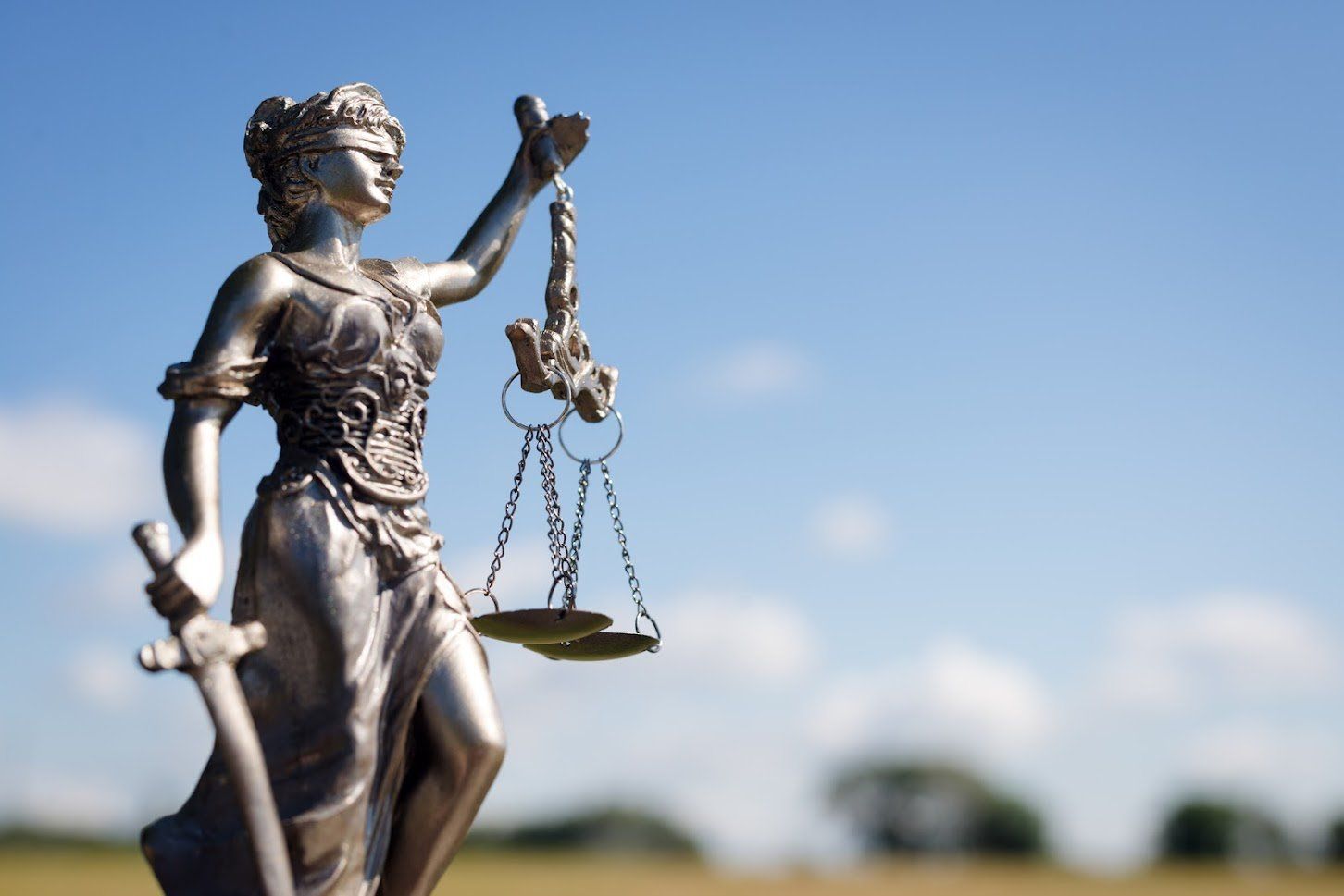 Statue of Lady Justice holding scales and sword, against a blue sky background.