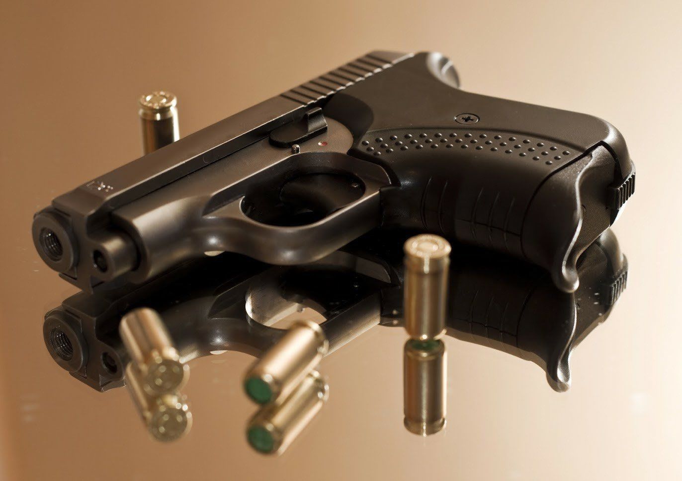 Black handgun and ammunition on a reflective surface.