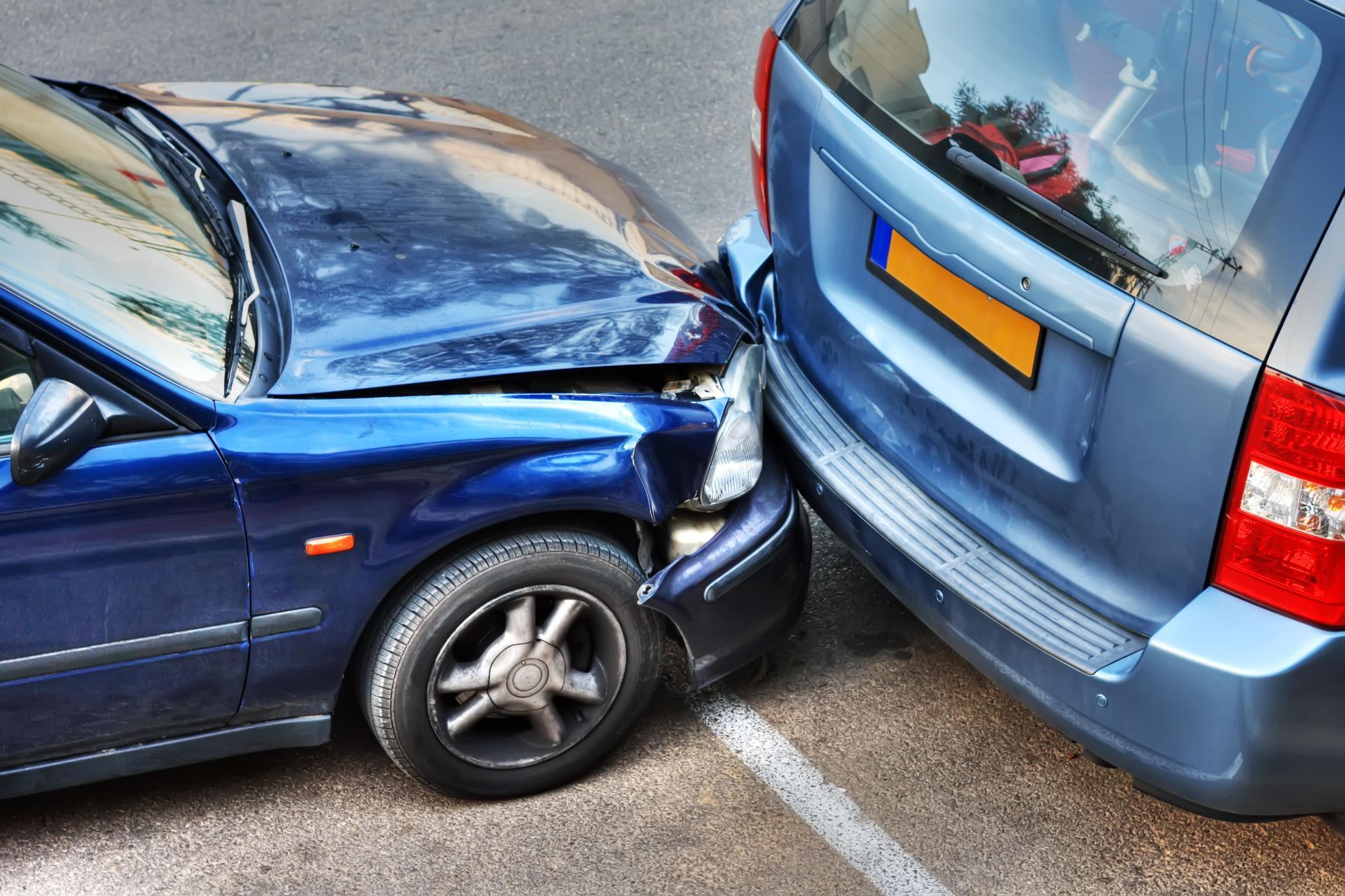 Two blue cars involved in a collision, damage on the front of one car, rear of the other.