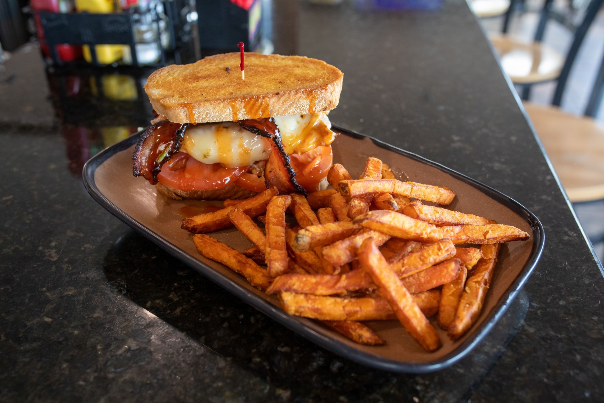 Sandwich with sweet potato fries on a plate. The sandwich has fried egg and bacon, and is held with a toothpick.