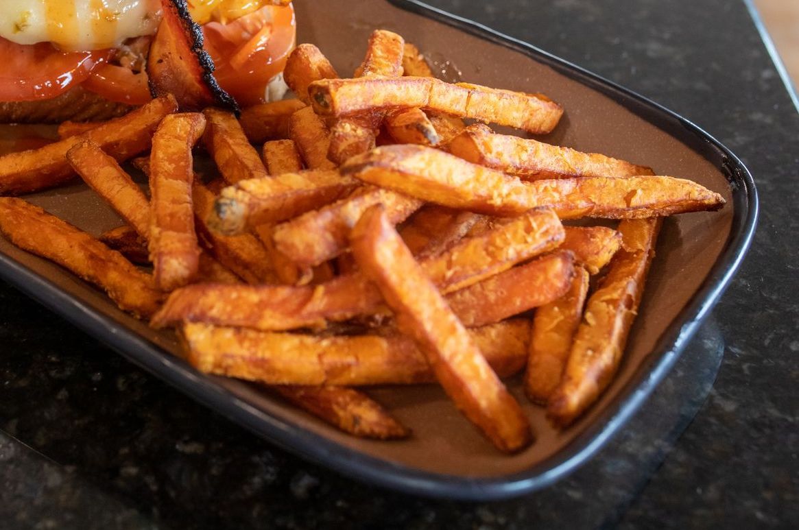Plate of sweet potato fries next to a burger with a tomato.