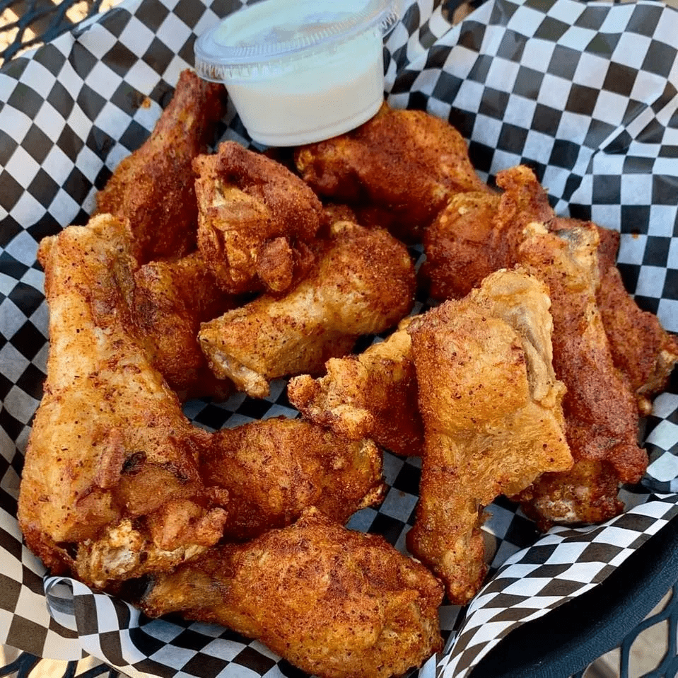 Pile of seasoned chicken wings with a side of white dipping sauce, on checkered paper in a basket.