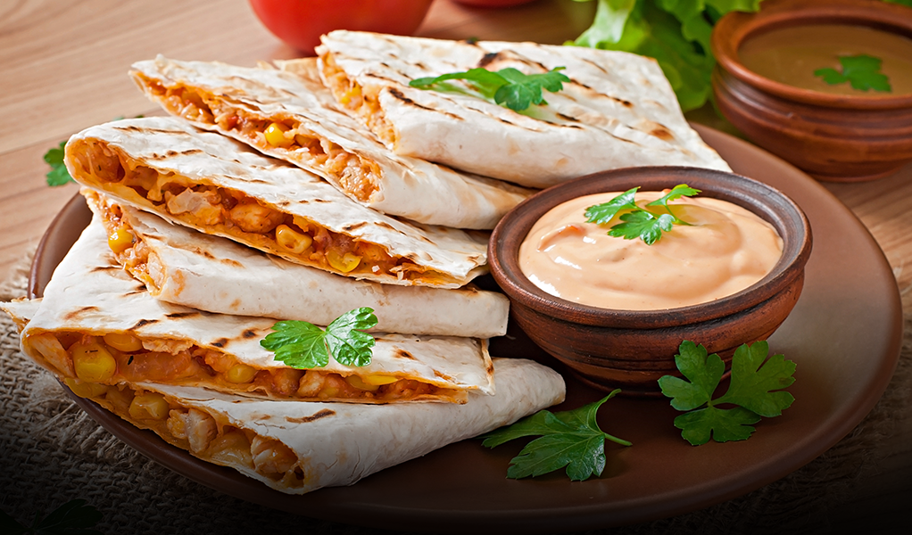 Quesadillas with filling, stacked on a plate with dipping sauce and parsley garnish.