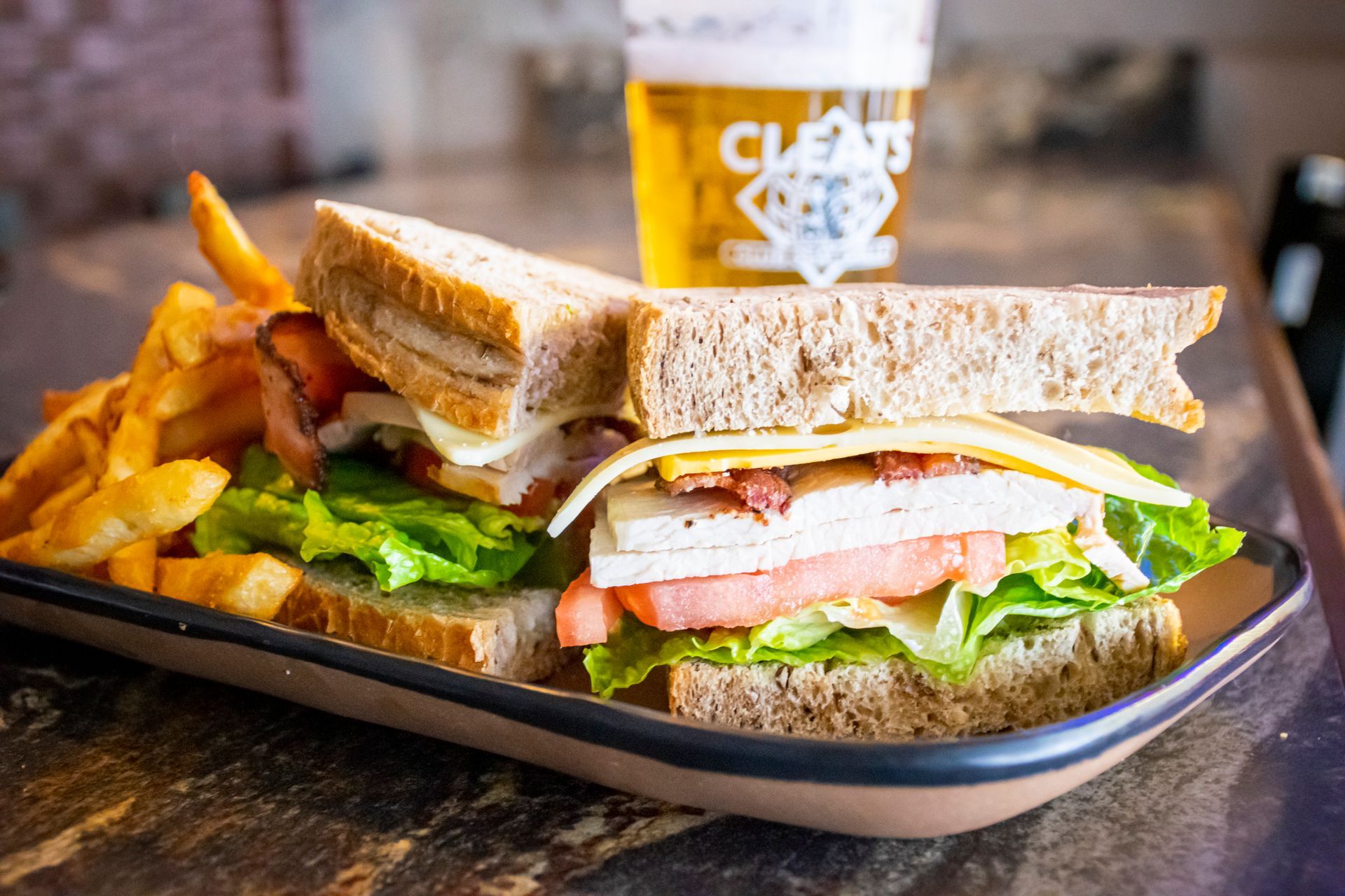 Sandwich with fries on a plate and a beer in the background.