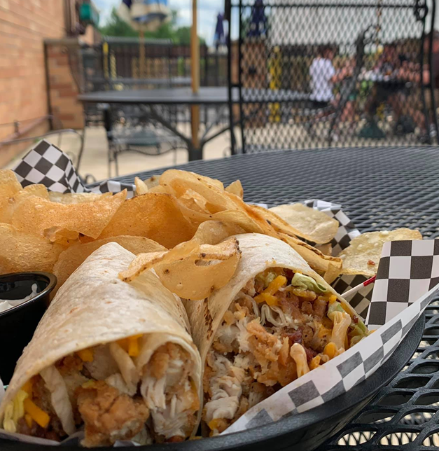 A chicken wrap and chips on a table at a restaurant patio.