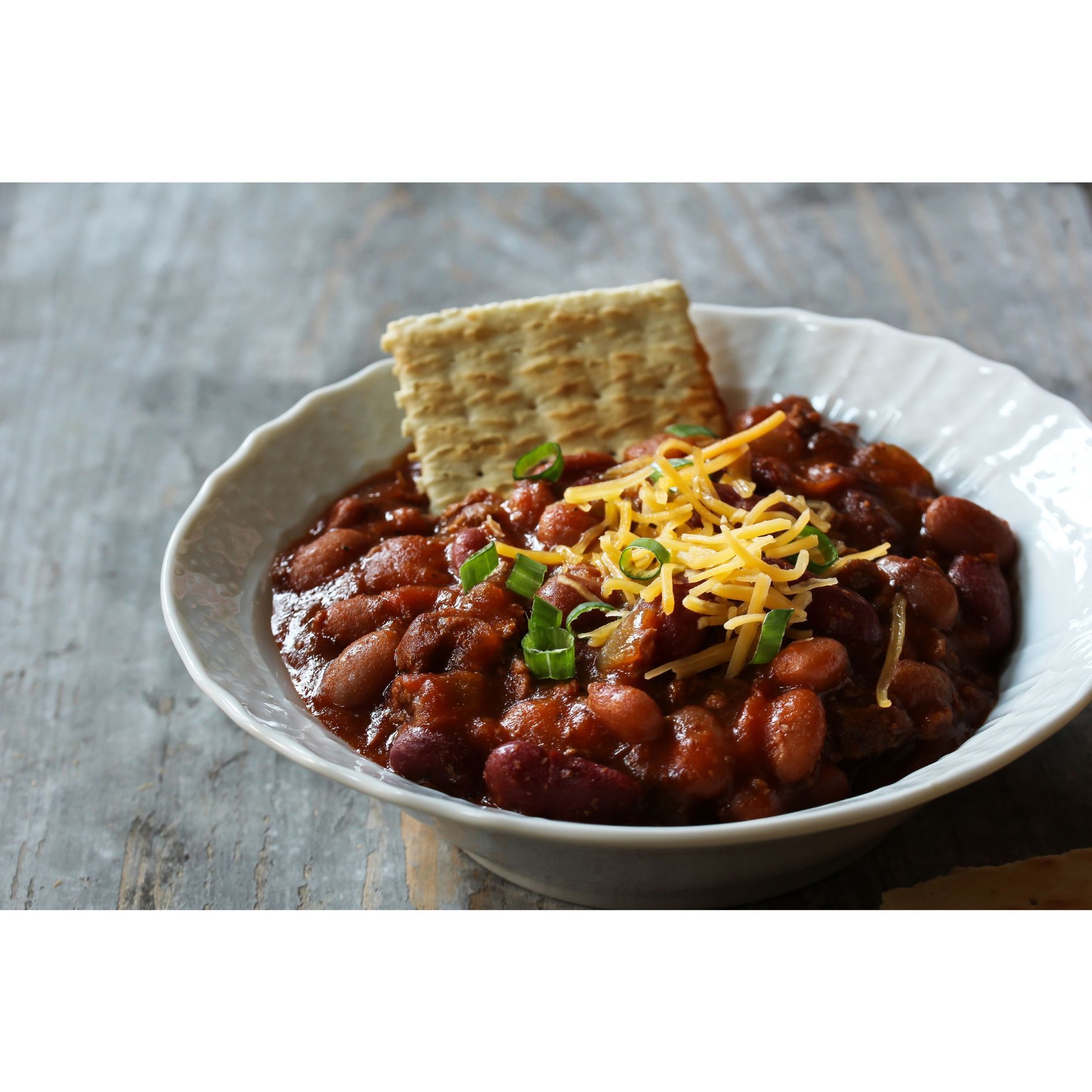 Bowl of chili with cheese, crackers, and green onions.