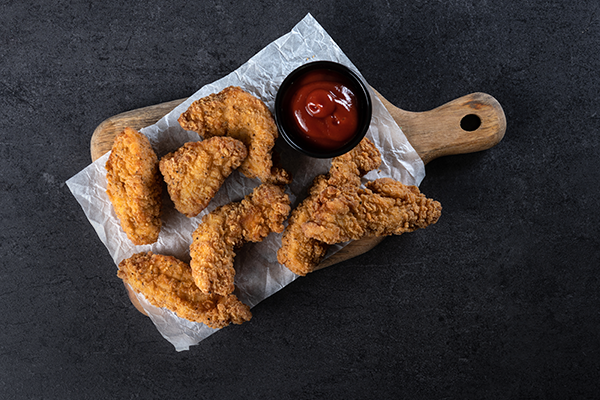 Fried chicken wings and ketchup in a small bowl on a wooden cutting board, dark background.