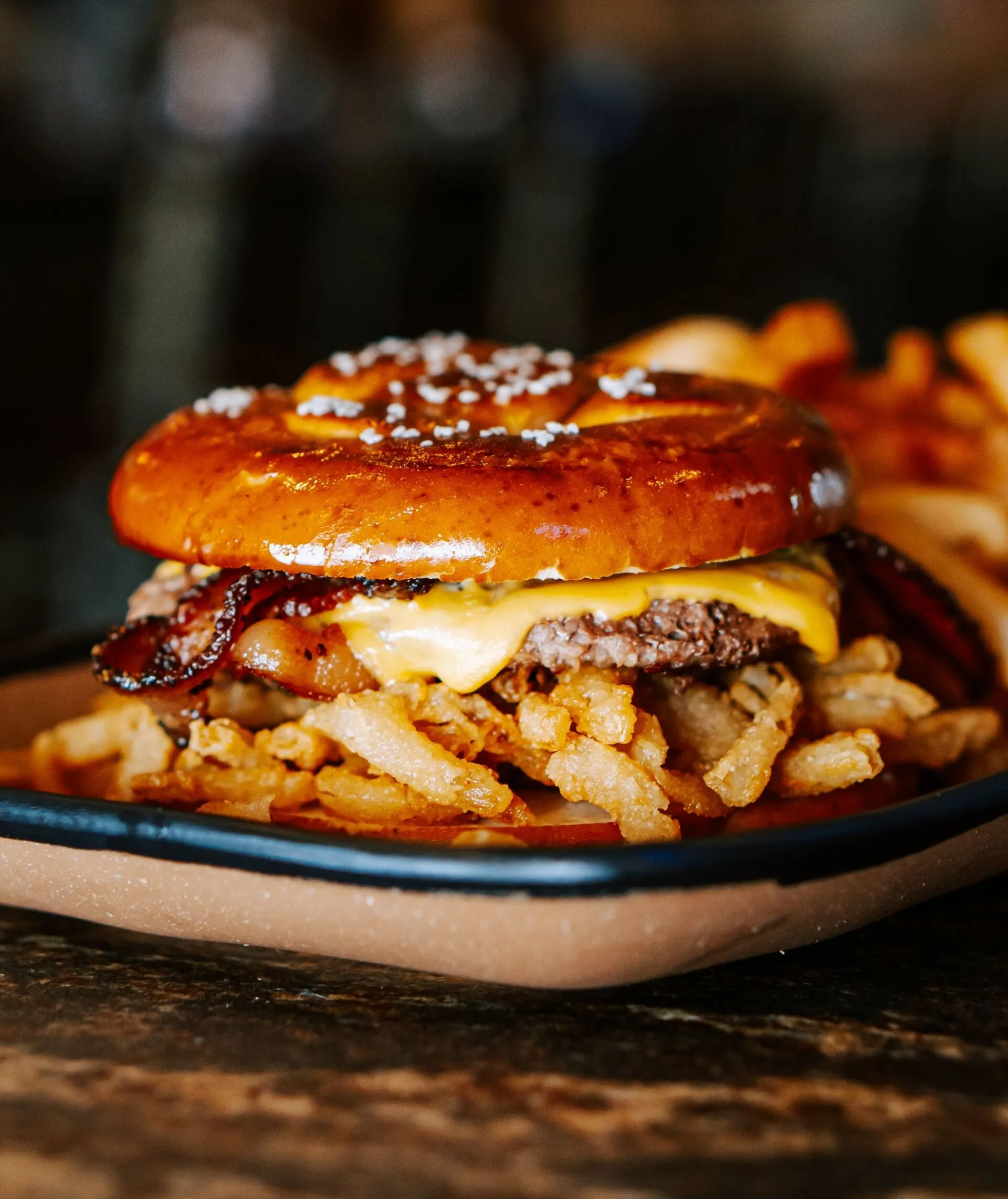 Hamburger with bacon, cheese, and onion straws on a pretzel bun, served with fries.