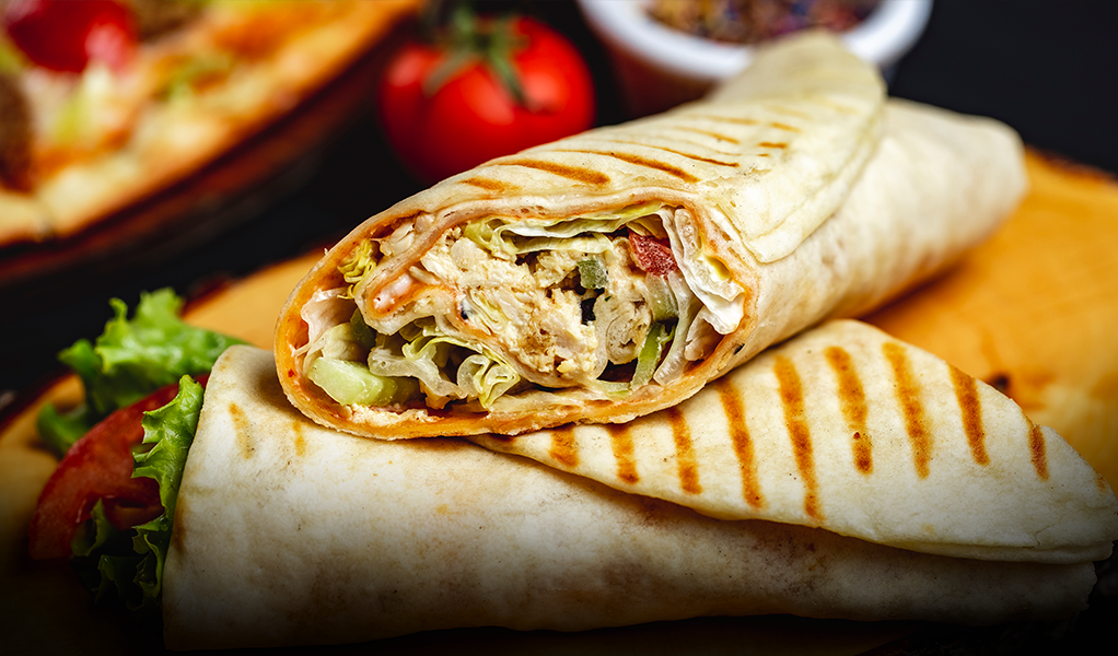 Grilled chicken wraps with lettuce, tomato, and sauce, on a wooden surface.