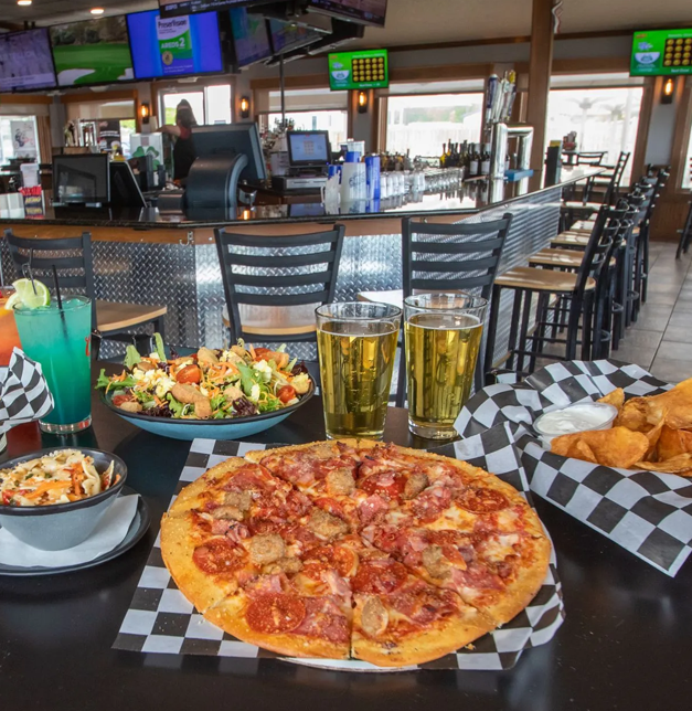 A table in a bar with food and drinks: pizza, salad, coleslaw, chips, and beer.