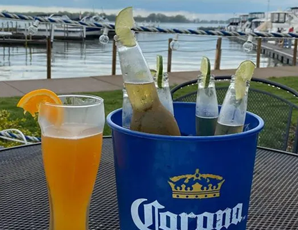 Beer bucket with limes, orange drink, waterfront scene.