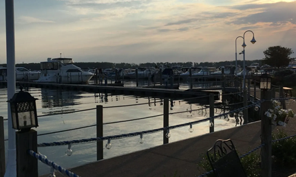 Marina with boats docked at dusk, water reflecting the sky. Wooden pier with lights in the foreground.