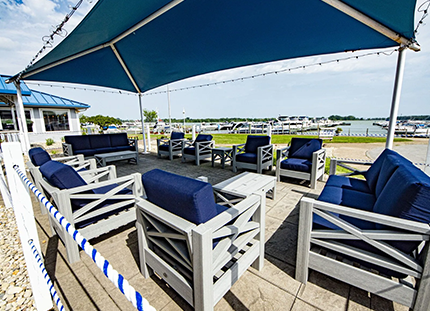 Outdoor patio seating under a blue canopy with a waterfront view. Gray furniture, blue cushions.