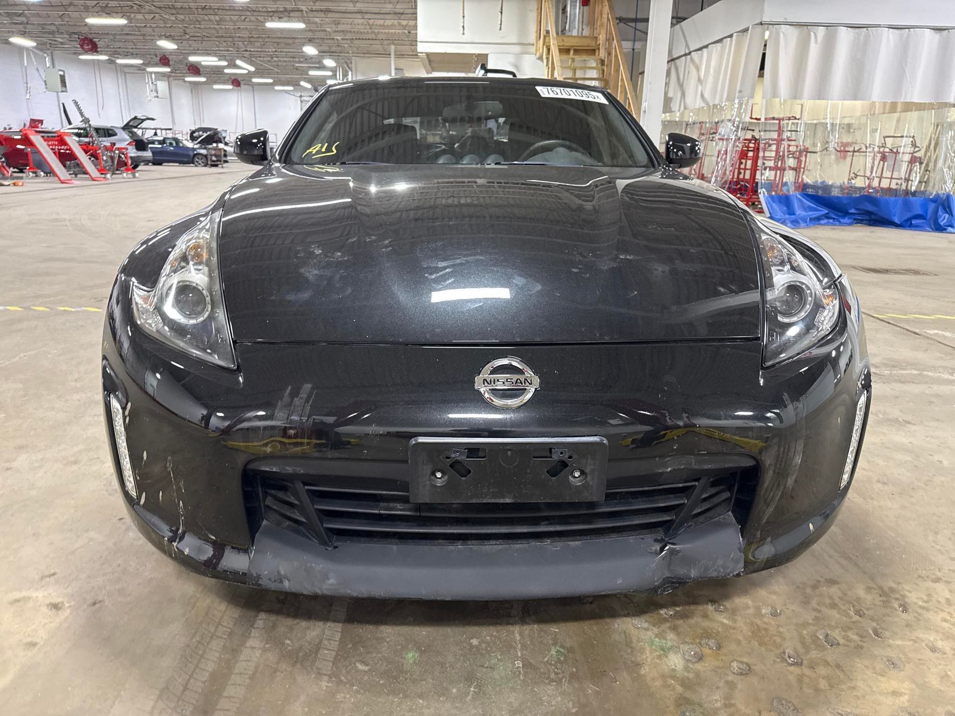 Black Nissan in a repair shop, showing collision damage on bottom bumper.