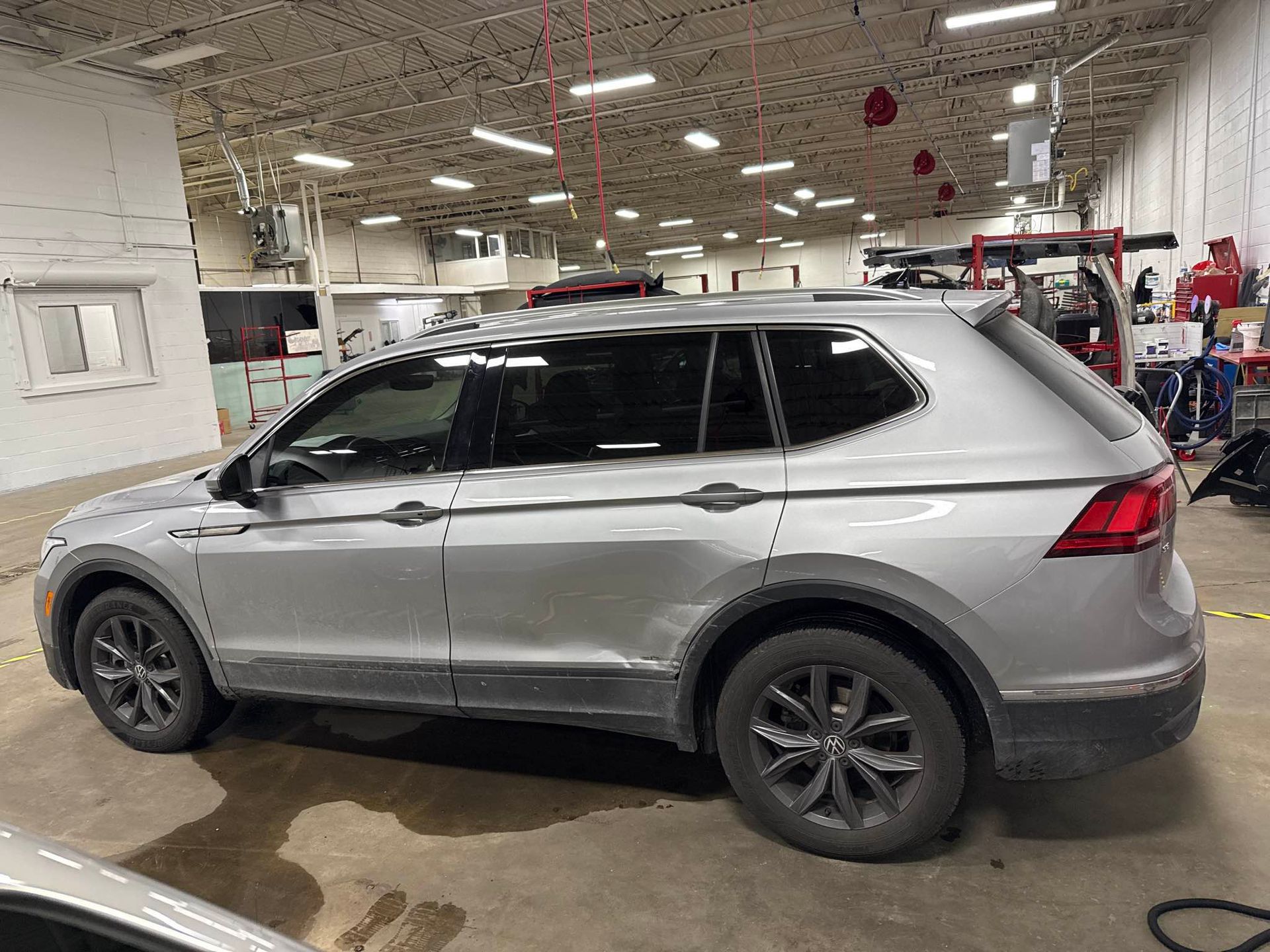 Silver Damaged Tiguan with large dent on backdoor parked inside of shop
