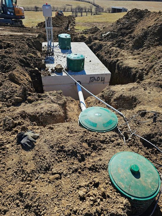 Septic system installation in dirt trench; concrete tank with green lids and piping.