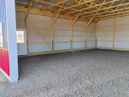 Interior of a new pole barn with wood framing, metal siding, gravel floor, and a door.