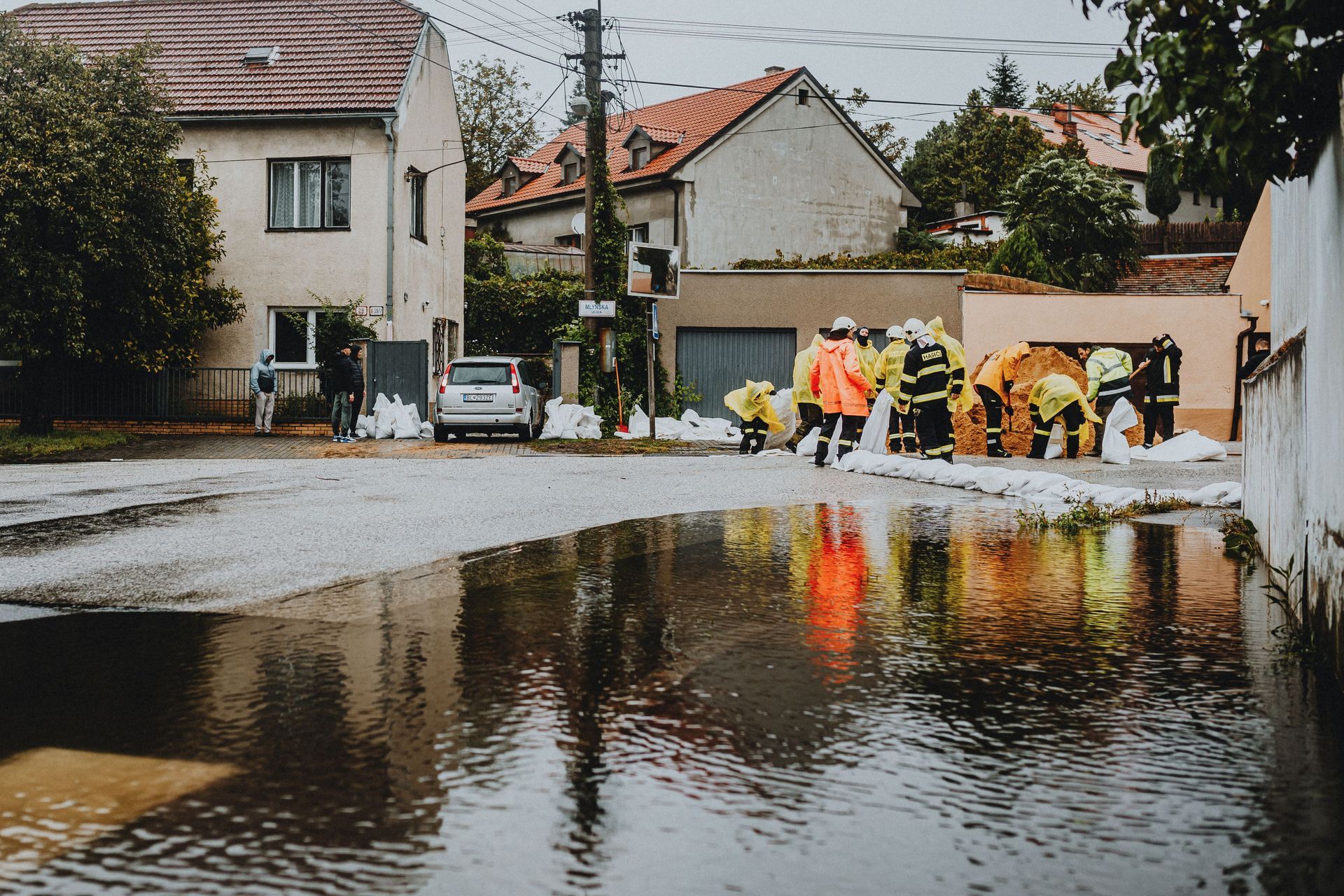 Workers in yellow rain gear clearing floodwater from a street in a residential neighborhood