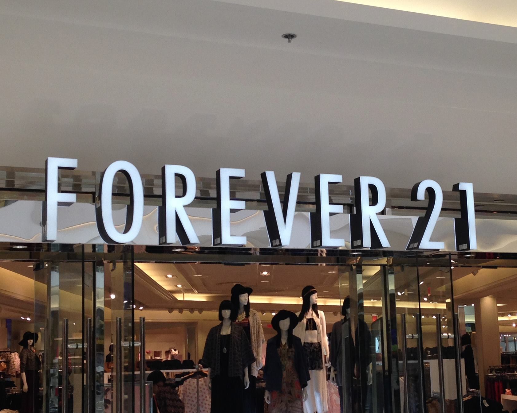 Forever 21 store entrance with mannequins in the window, under a large white and black sign. Forever 21 store entrance with mannequins in the window, under a large white and black sign.